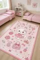 Pembe çocuk odası halısı üzerinde elbiseli kedi, fiyonk, kalp, çanta ve taç motifleri yer alır